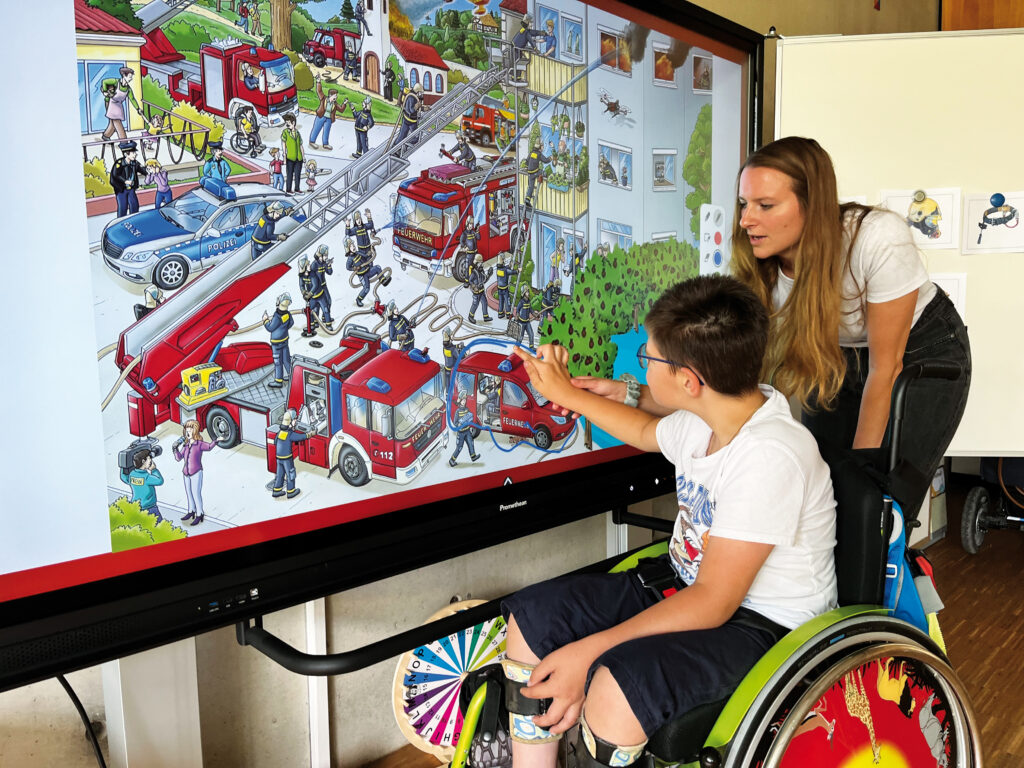 Ein Junge im Rollstuhl lernt zusammen mit einer Frau an einer interaktiven Tafel.